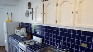 A kitchen with white cabinets, a blue tiled backsplash, a stove, a sink, and a microwave.