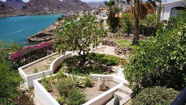 A landscaped garden with a cactus, a stone planter, and a view of a coastal town with mountains in the background.