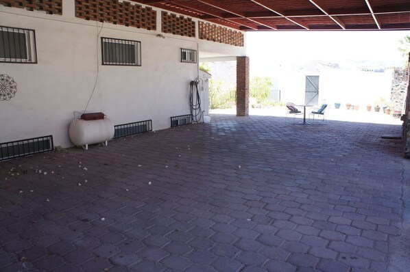 An outdoor patio area with a brick floor, a white wall with a decorative pattern, and a covered section with a red roof.