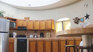 A kitchen with wooden cabinets, a stainless steel refrigerator, a microwave, an oven, and a coffee maker. There is a curved island with stools and a decorative glass piece. - Costa del Mar 57 2 Bedroom Apartment By Seaside San Carlos (San Carlos)