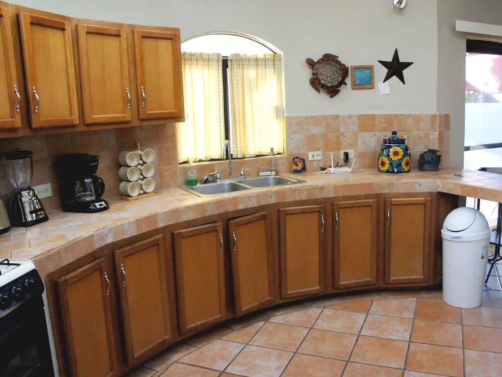 Una cocina con gabinetes de madera, estufa, fregadero y un bote de basura.