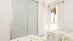 Een kamer met een schuifdeur van glas, een raam met uitzicht op bomen, en een tafel met een tafelkleed met bloemen.