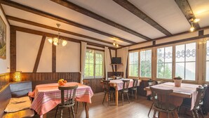 Un coin repas chaleureux avec des poutres en bois, des tables recouvertes de nappes roses et des chaises.