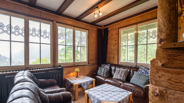 L’intérieur chaleureux d’un chalet avec un canapé en cuir, une table en bois et de grandes fenêtres donnant sur le paysage extérieur.
