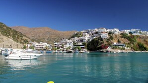 Un pueblo costero con edificios en una colina, barcos amarrados en el agua y un cielo azul despejado.