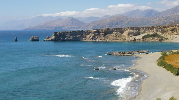 Un paisaje costero con vistas claras al mar, acantilados rocosos y una playa de arena.