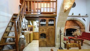 A rustic interior with a wooden staircase, a loft bedroom, a fireplace, and traditional wooden furniture. - Villa in Crete with Vineyard Experience (Kalamitsi Alexandrou)