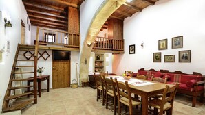 A rustic interior with a wooden dining table, red sofa, and a loft area with a wooden staircase. - Villa in Crete with Vineyard Experience (Kalamitsi Alexandrou)
