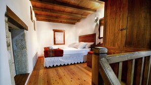A bedroom with a wooden floor, a bed with a white bedspread, a wooden headboard, and a wooden wardrobe. - Villa in Crete with Vineyard Experience (Kalamitsi Alexandrou)