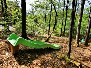 Eine grüne Rutsche in einer bewaldeten Gegend mit Bäumen und einer Holzbank in der Nähe.