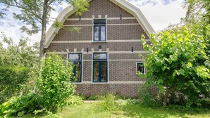 A two-story brick house with a gabled roof, multiple windows, and surrounded by lush greenery. - Holiday home in Krabbendam (Krabbendam)