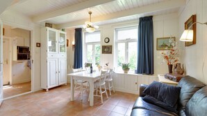 A room with a dining table, chairs, a black leather sofa, a window with curtains, a clock, and a small table with a vase of flowers. - Holiday home in Krabbendam (Krabbendam)