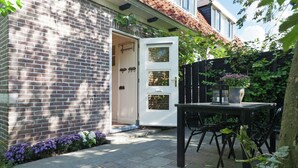 A brick house with a white door, a small patio with a table and chairs, and a garden with purple flowers. - Holiday home in Krabbendam (Krabbendam)