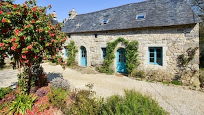 Un bâtiment en pierre avec un toit en pente, deux fenêtres en arc de cercle et une porte bleue.