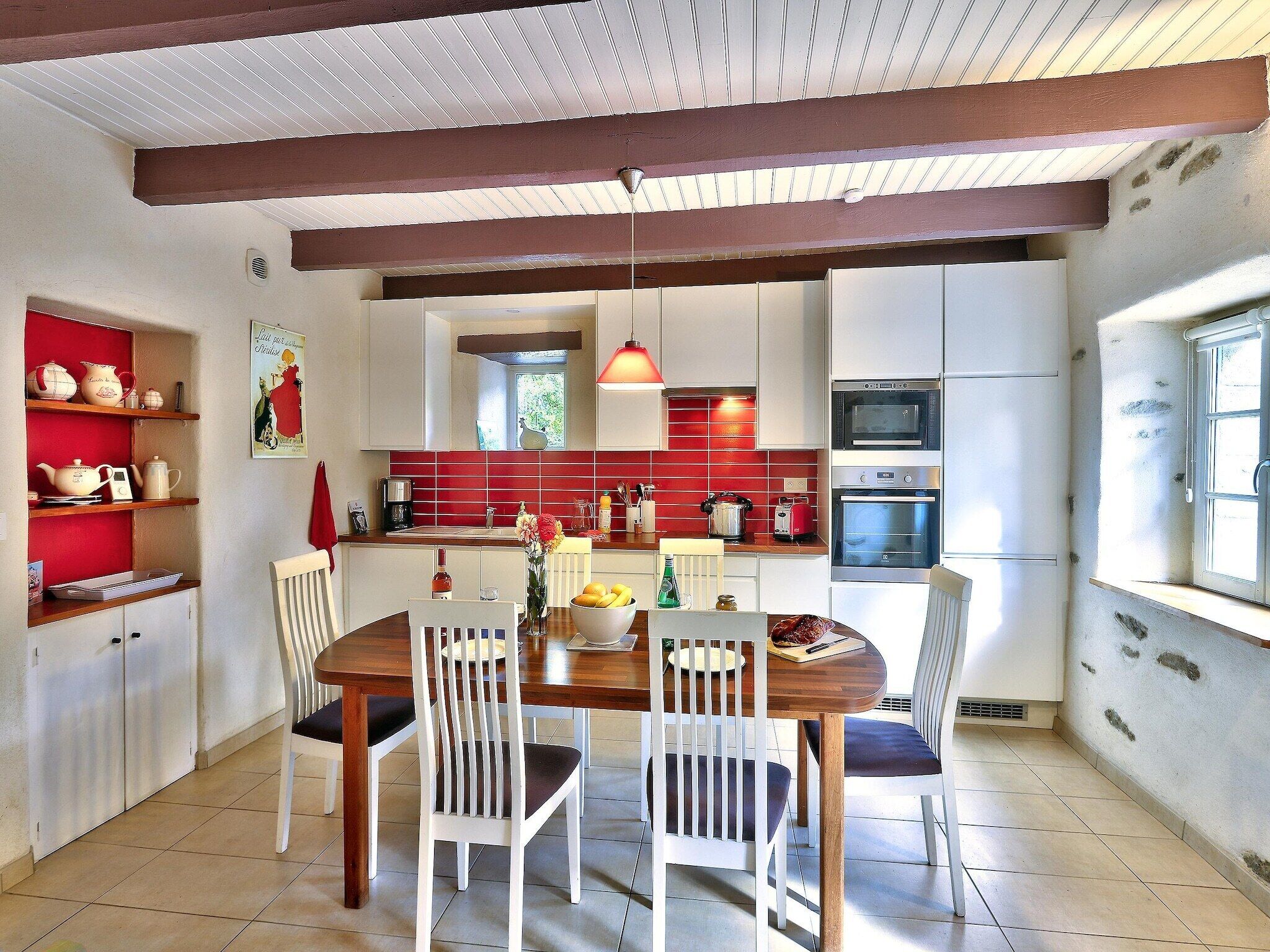 A kitchen with white cabinets, a red backsplash, and a dining area with a wooden table and white chairs.