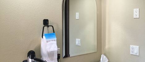 A hotel bathroom with a sink, mirror, towel rack, and a hairdryer.