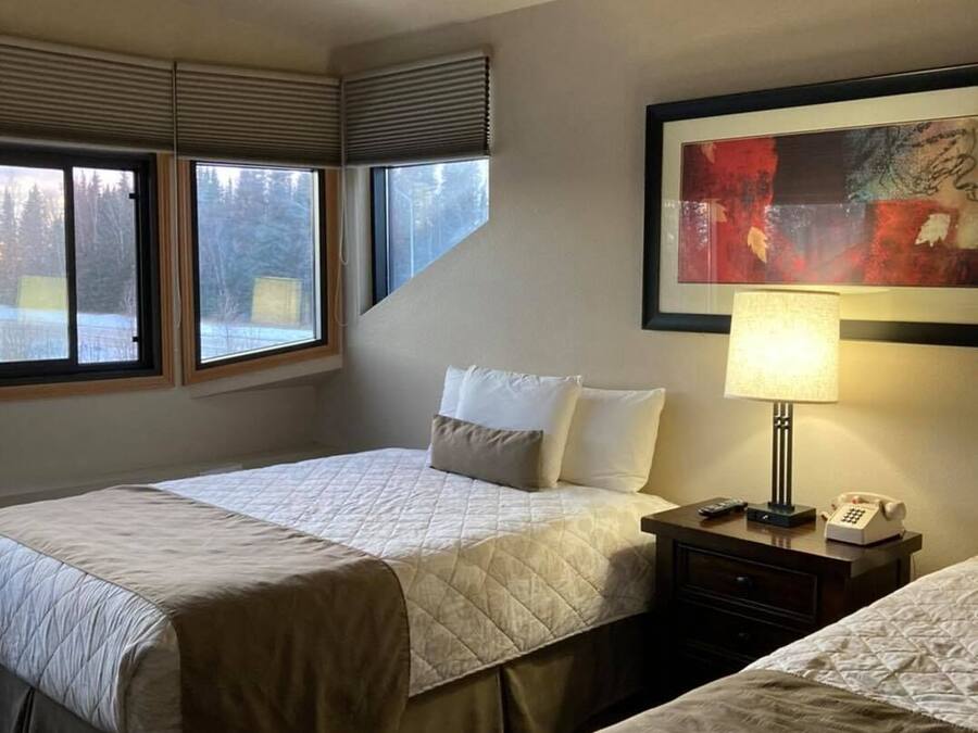 Habitación de hotel con dos camas, ventilador de techo, un cuadro en la pared y una ventana con persianas.