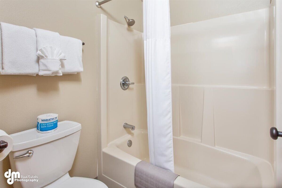 Een badkamer met een toilet, een bad en een douche. Er ligt een rol toiletpapier op het toilet.