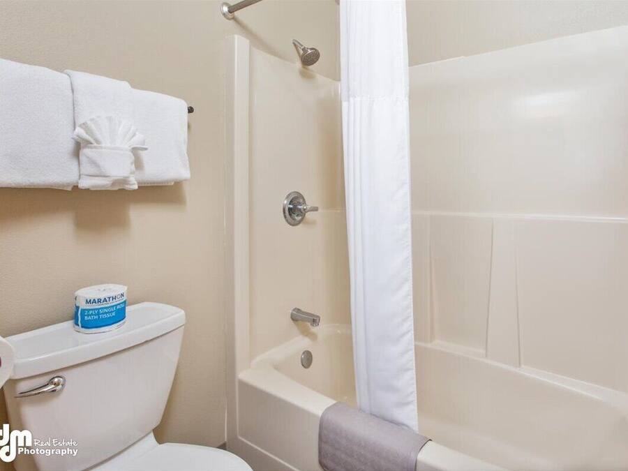 A bathroom with a toilet, a bathtub, and a shower. There is a roll of bath tissue on the toilet.