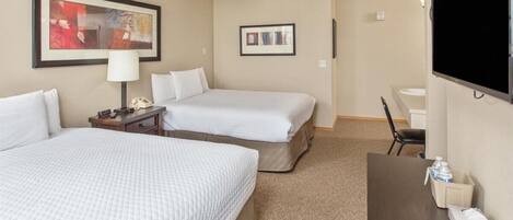 A hotel room with two beds, a desk, a chair, a TV, and a ceiling fan.