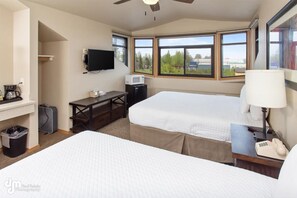 Ein Hotelzimmer mit zwei Betten, einem Schreibtisch, einem Fernseher und großen Fenstern mit Blick ins Freie.