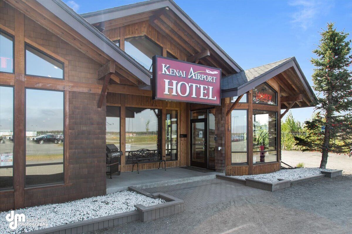 The exterior of the Kenai Airport Hotel with a prominent sign, large windows, and a gravel-paved entrance.