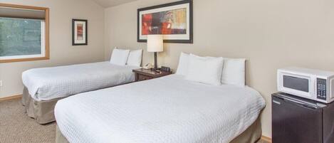 A hotel room with two beds, a ceiling fan, a painting, a lamp, and a microwave.