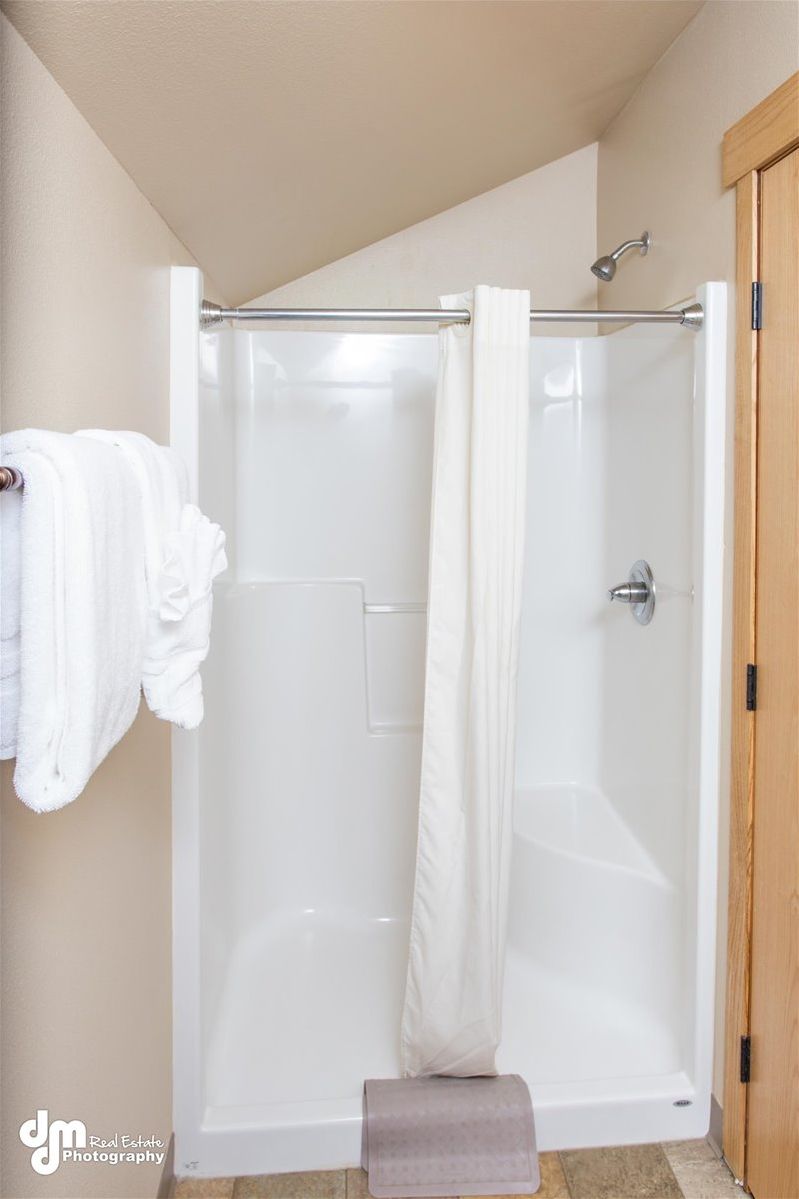 A walk-in shower with a glass door, a towel rack with a white towel, and a wooden door to the right.