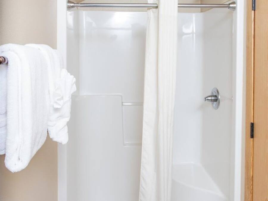 Ducha a pie con puerta de vidrio, un perchero con una toalla blanca y una puerta de madera a la derecha.