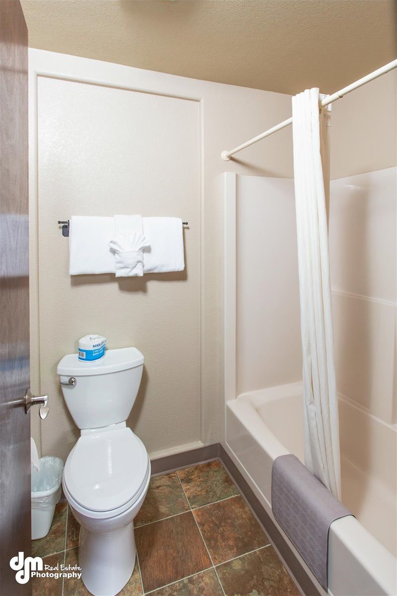 A bathroom with a toilet, a towel rack with a towel, a bathtub with a shower curtain, and a trash bin.