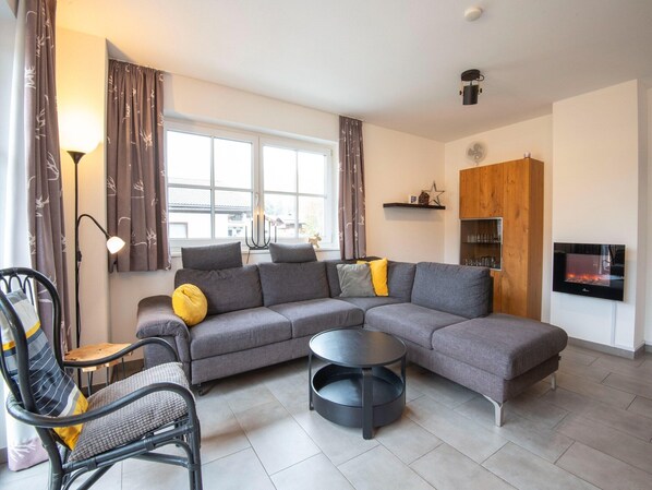 A modern living room with a grey sectional sofa, a round black coffee table, a black metal chair, and a wooden cabinet with shelves. - Apartment near the ski slope in Brixen (Brixen im Thale)