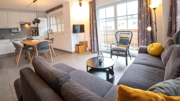 A modern living room with a sofa, armchair, and dining area. - Apartment near the ski slope in Brixen (Brixen im Thale)