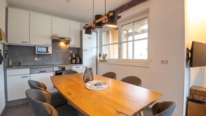 A modern kitchen with white cabinets, a wooden dining table, and grey chairs. - Apartment near the ski slope in Brixen (Brixen im Thale)