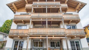 A multi-story building with wooden balconies, a covered outdoor seating area, and a stone facade. - Apartment near the ski slope in Brixen (Brixen im Thale)