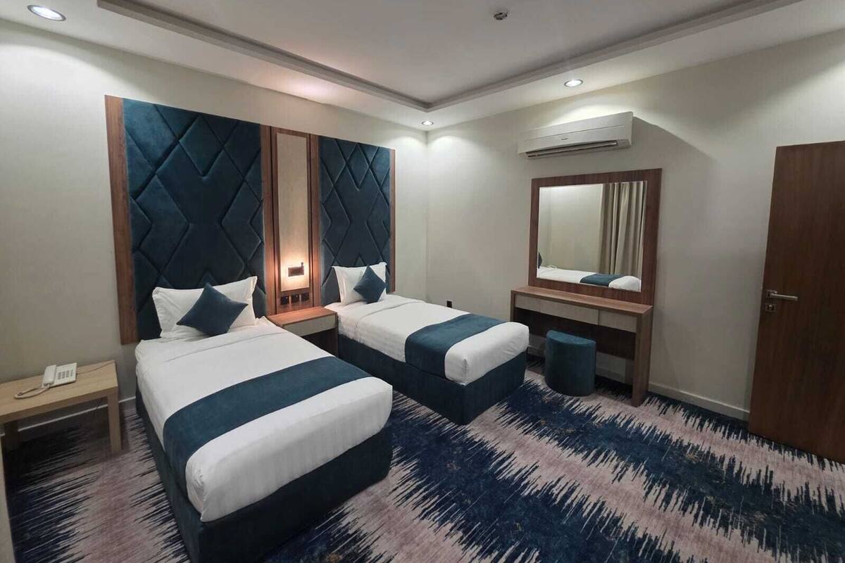 A hotel room with two beds, a large mirror, a small trash bin, and a telephone on a nightstand.