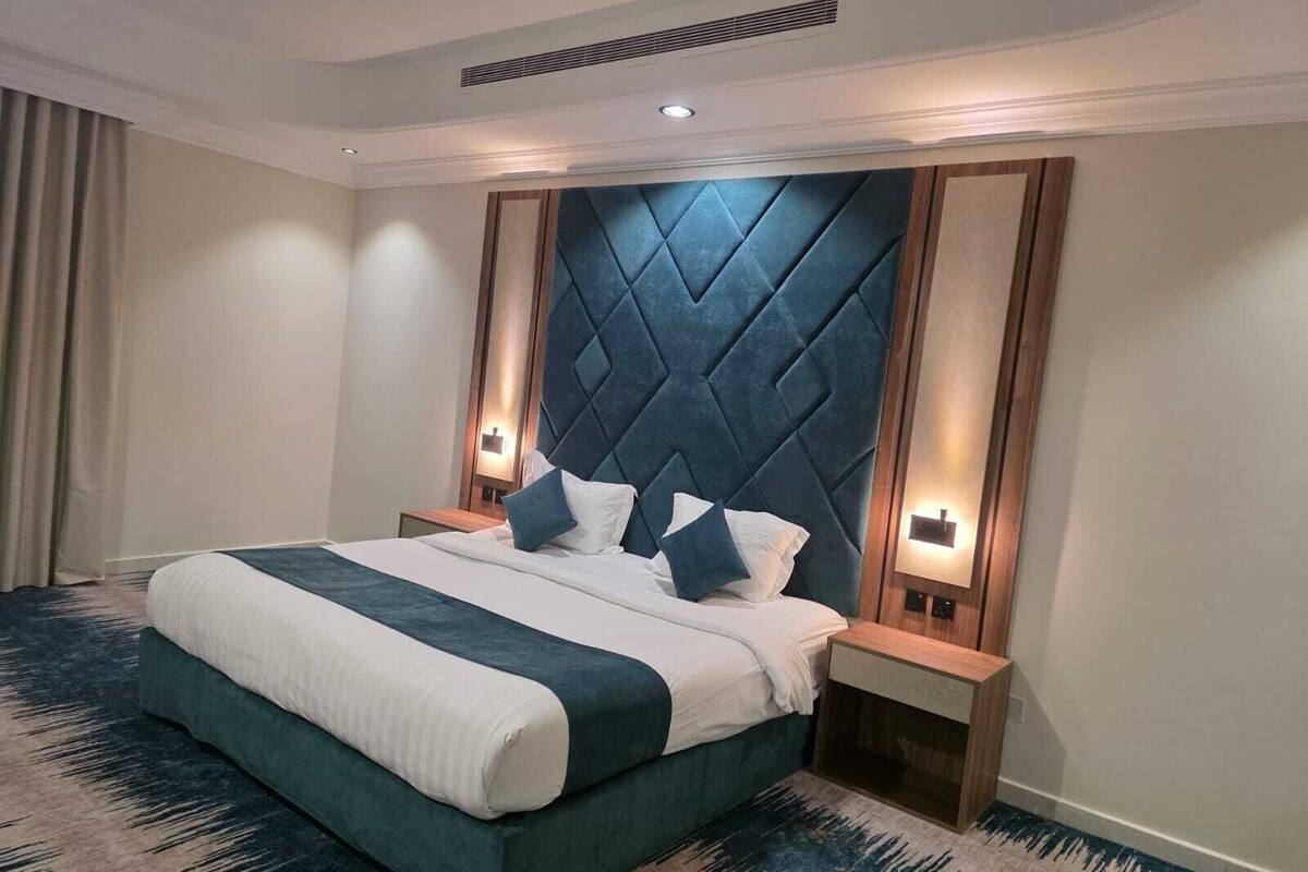 A hotel room with a large bed, two bedside tables, a modern headboard, and a patterned carpet.