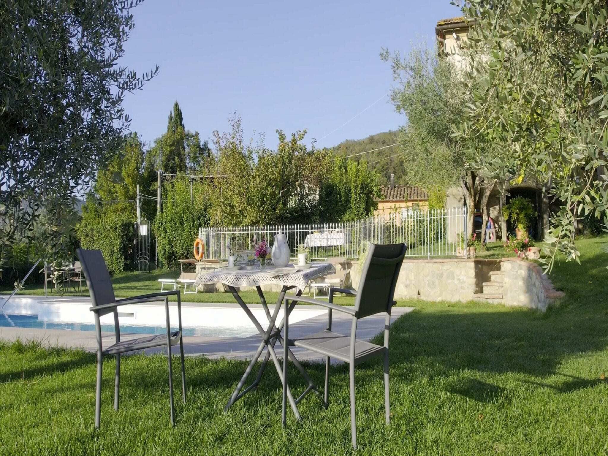 Area piscina con tavolo e sedie, circondata da vegetazione e un muro in pietra.