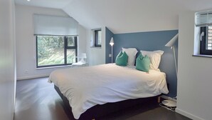 Une chambre moderne avec un grand lit, une vue sur la verdure et une lucarne.