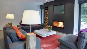 Un salon moderne avec une cheminée, des canapés gris, une table basse blanche et un tapis rouge.