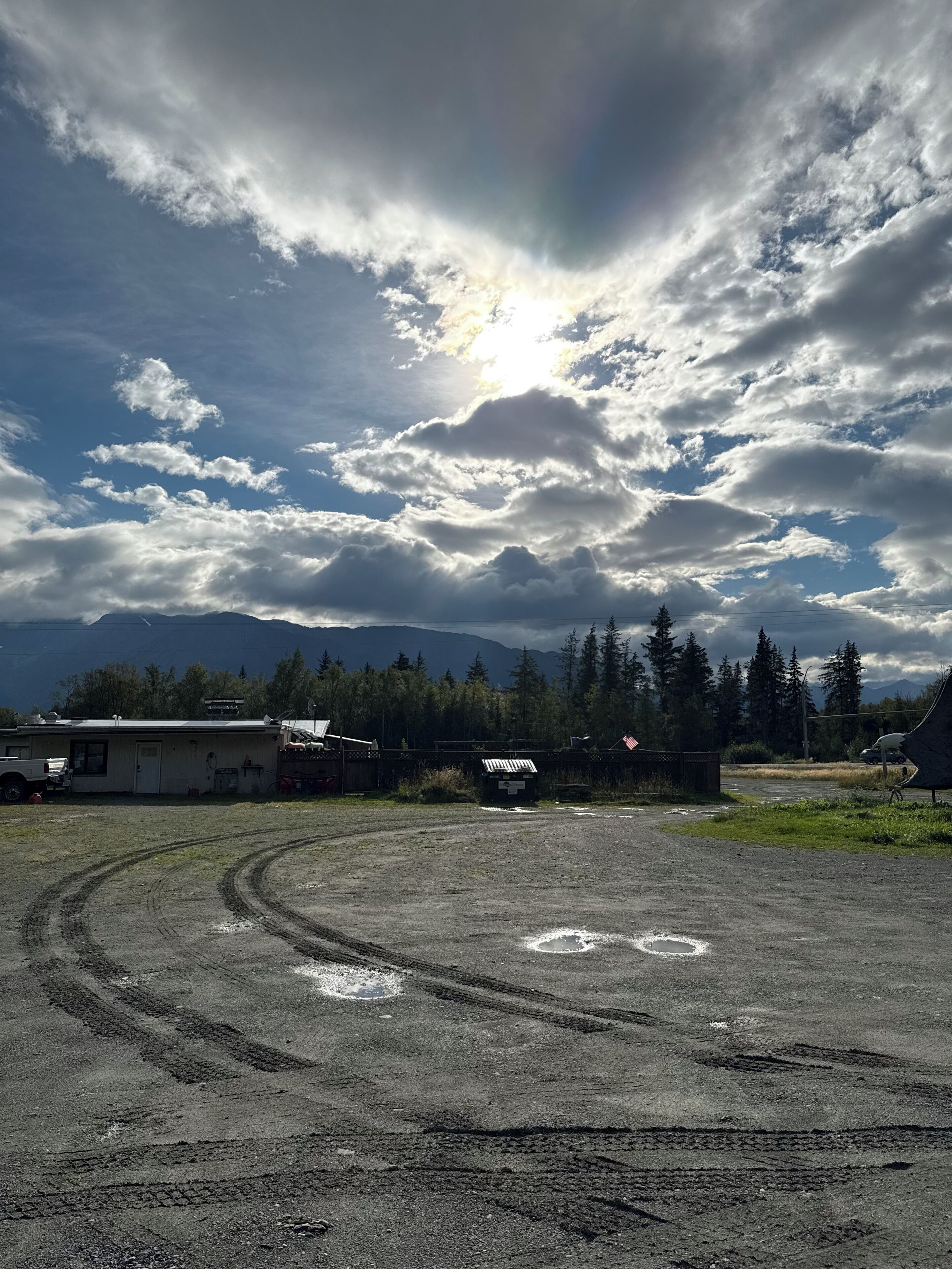 A parking lot with tire tracks, a building, and a forested area in the background.