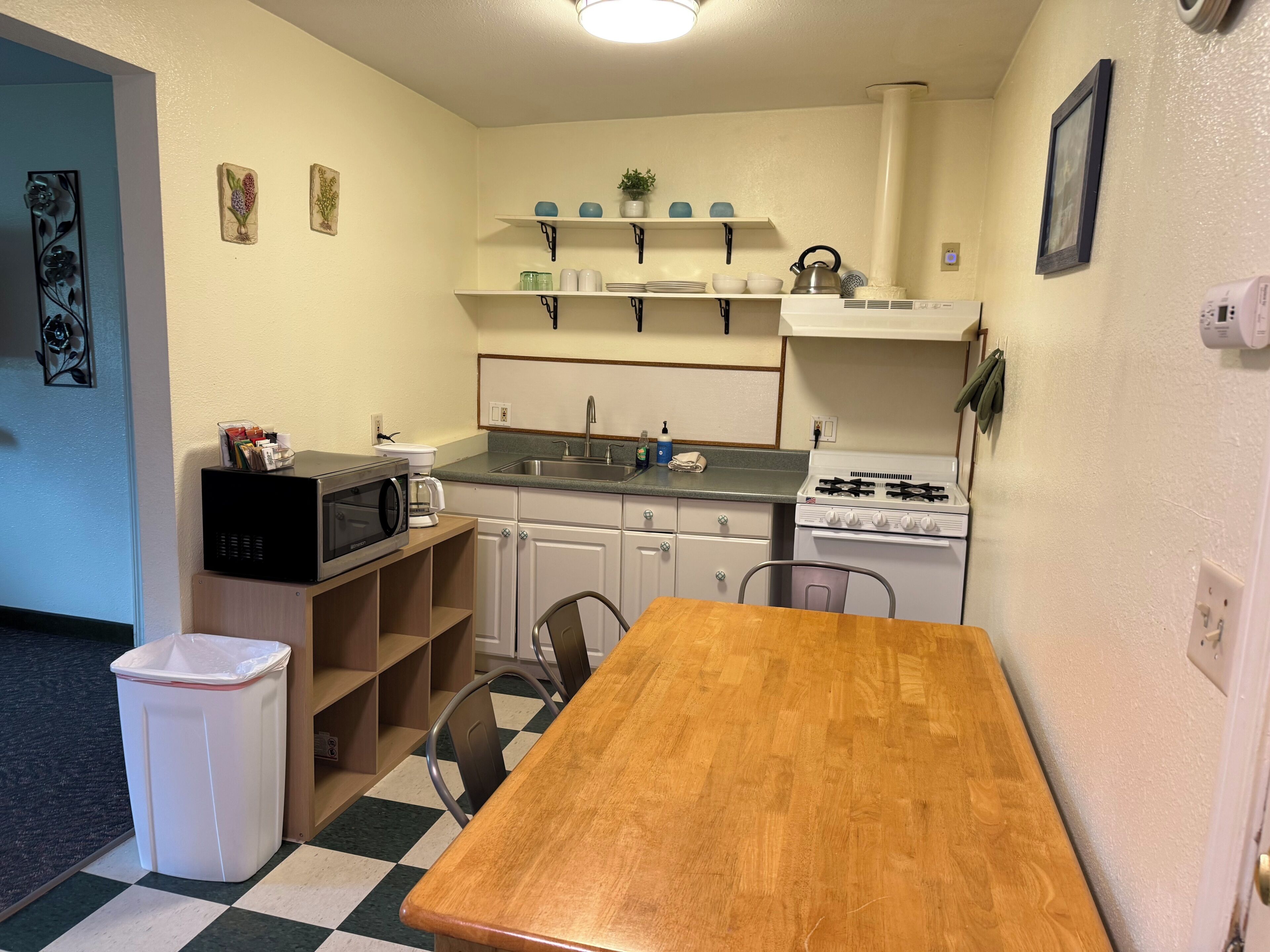 A compact kitchen with a wooden table, a microwave, a stove, and a trash bin.