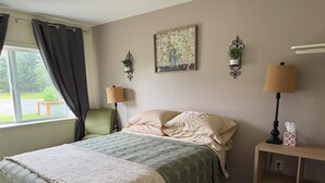 A room with a bed, two wall-mounted lamps, a small bedside table with a tissue box, a chair, and a window with curtains. - Bird Creek Motel (Indian)