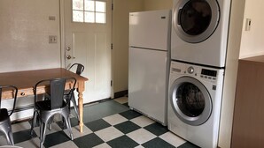 A compact kitchen with a dining table, chairs, a refrigerator, and a stacked washer and dryer. - Bird Creek Motel (Indian)