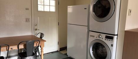 A compact kitchen with a dining table, chairs, a refrigerator, and a stacked washer and dryer.