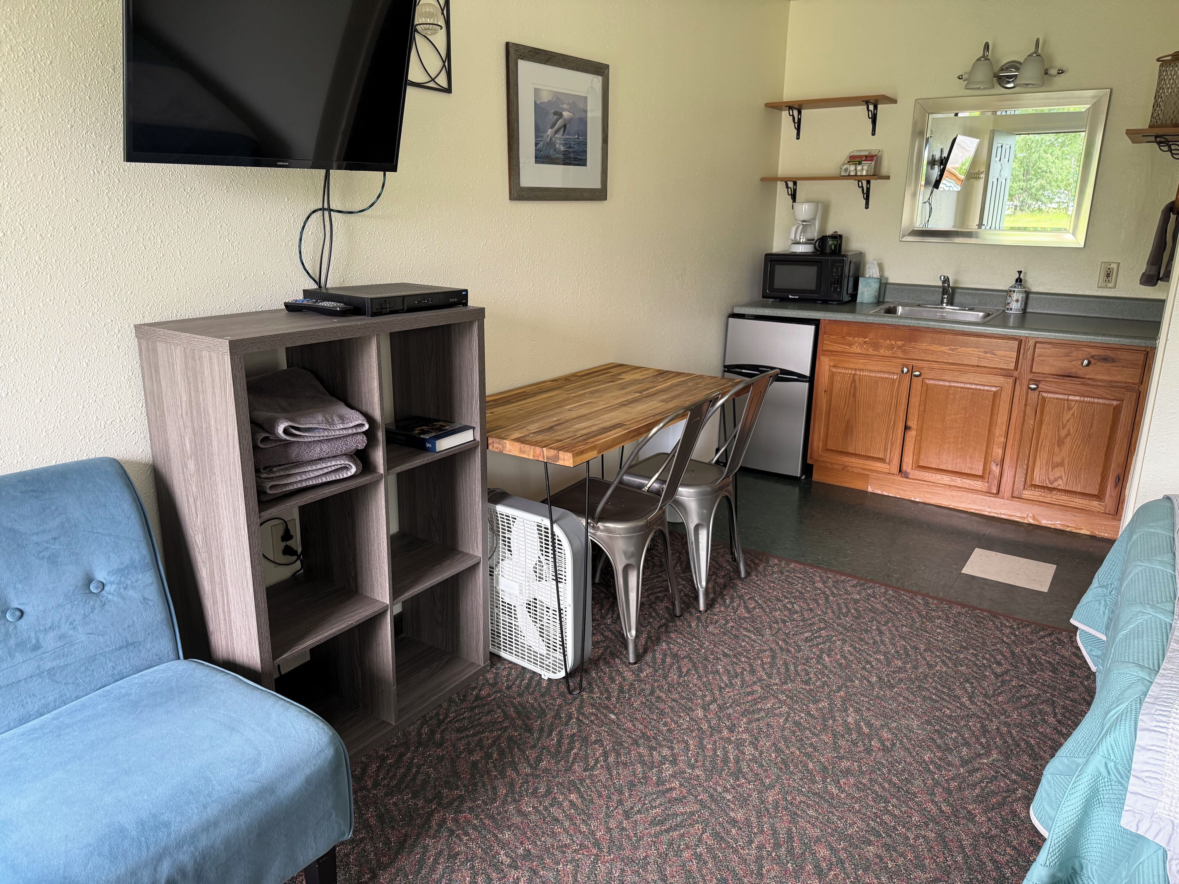 Un espacio habitable compacto con sofá, una mesa de madera, kitchenette y televisión montada en la pared.