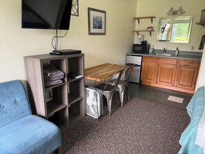 A compact living space with a sofa, a wooden table, a kitchenette, and a television mounted on the wall. - Bird Creek Motel (Indian)
