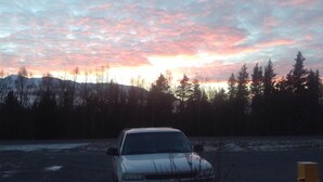 A car parked in a lot with a forest and mountains in the background. - Bird Creek Motel (Indian)