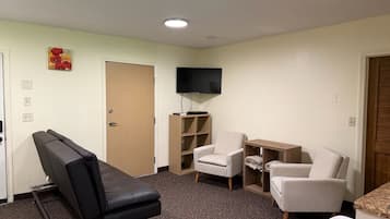 A room with a massage chair, two armchairs, a TV, and a small wooden table.