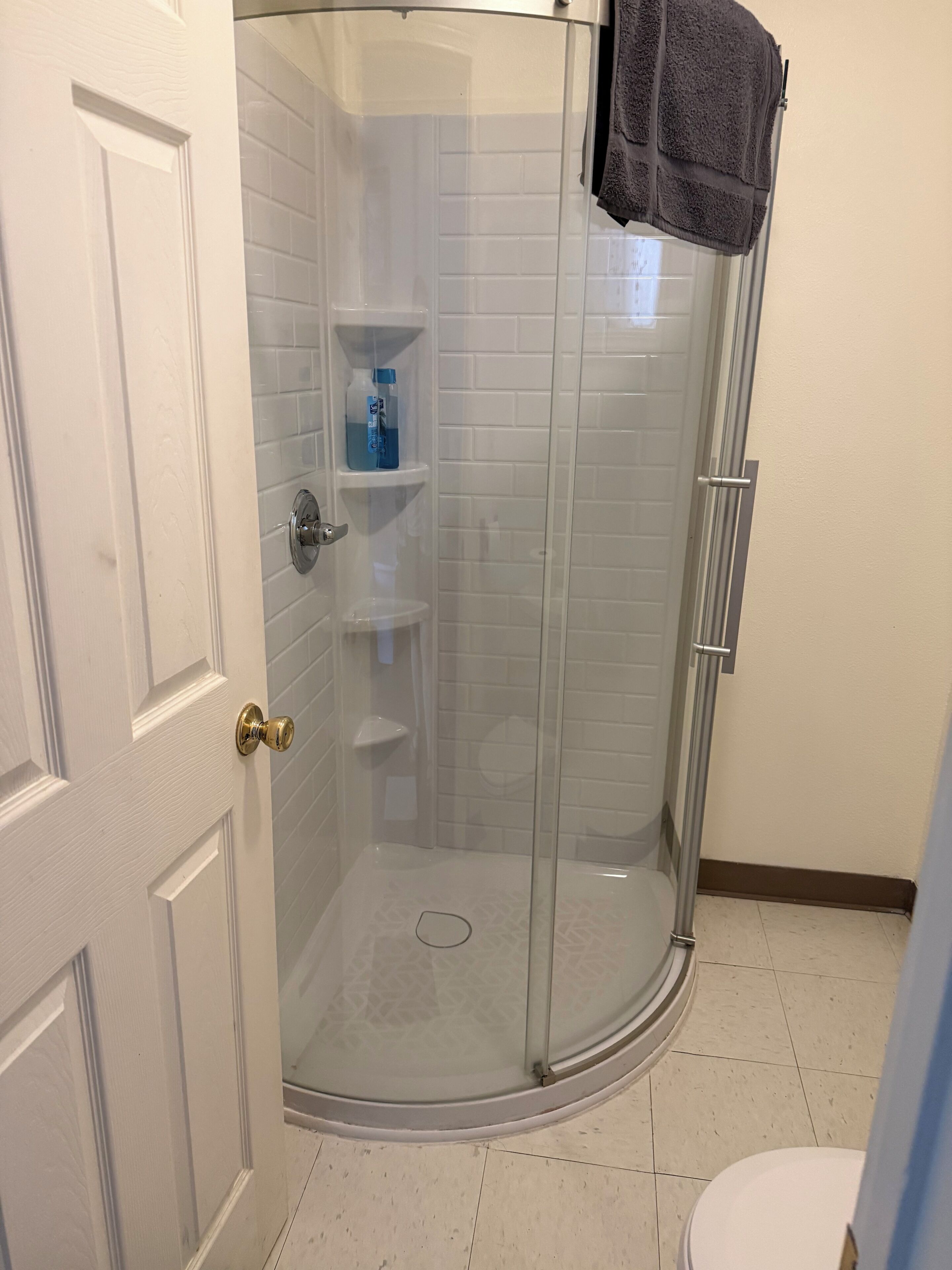 A bathroom with a glass shower enclosure, white tiled walls, a white toilet, and a towel hanging on the shower door.