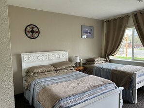 A bedroom with two beds, a nightstand, a wall clock, a framed picture, and a window with curtains. - Bird Creek Motel (Indian)